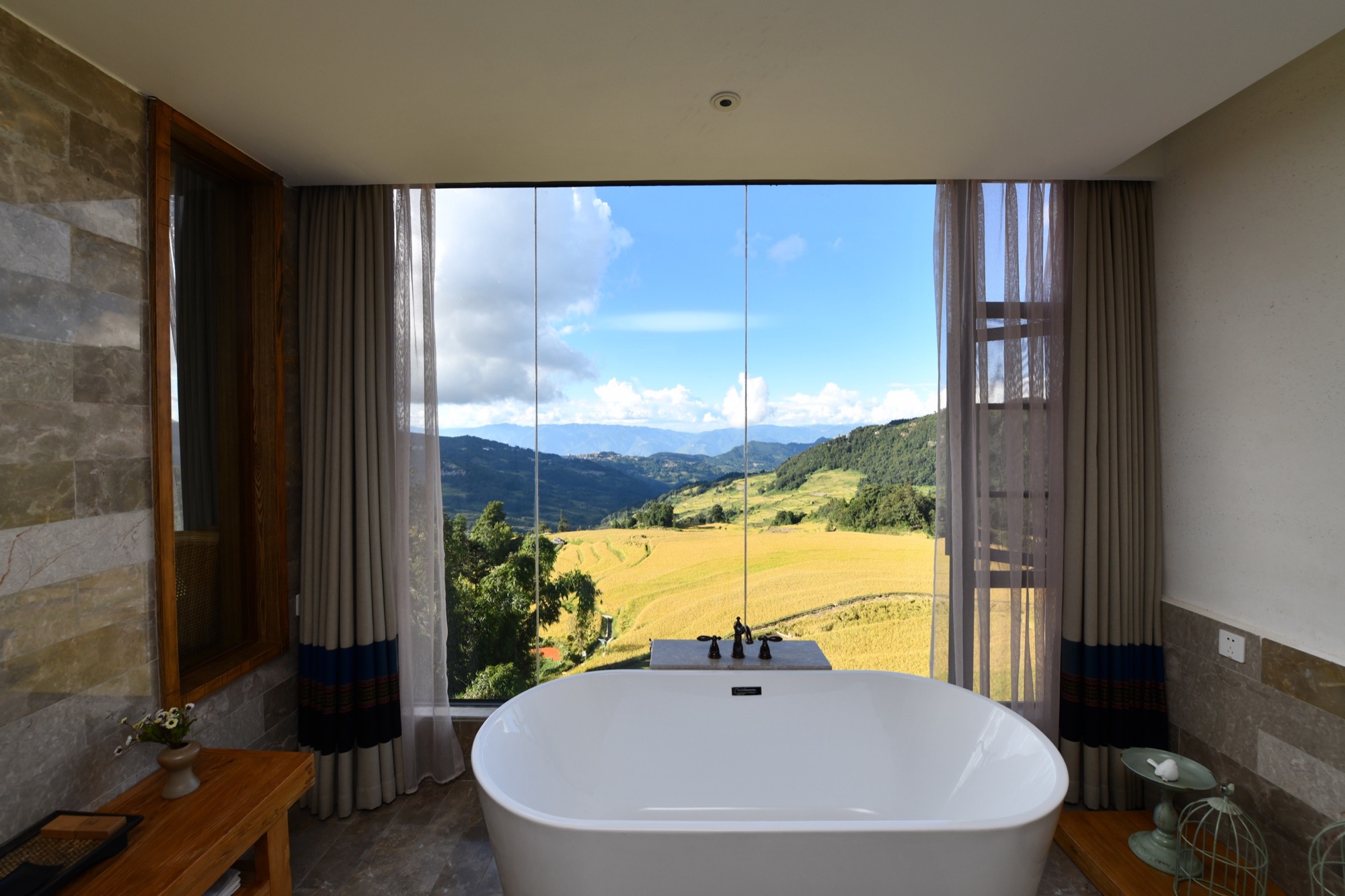 A freestanding bathtub in a stargazing room facing golden rice fields and the mountains of Yuanyang